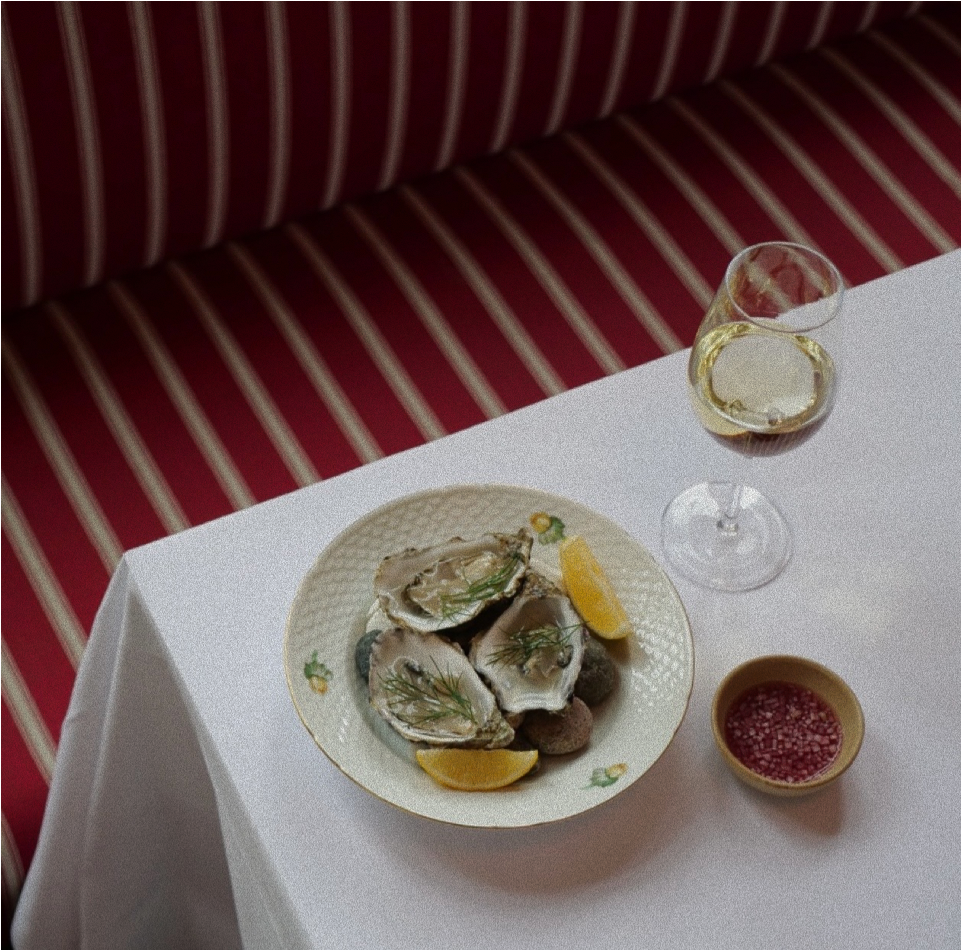 Oysters with lemon and dill and a glass of white wine on a white tablecloth at a Madklubben restaurant
